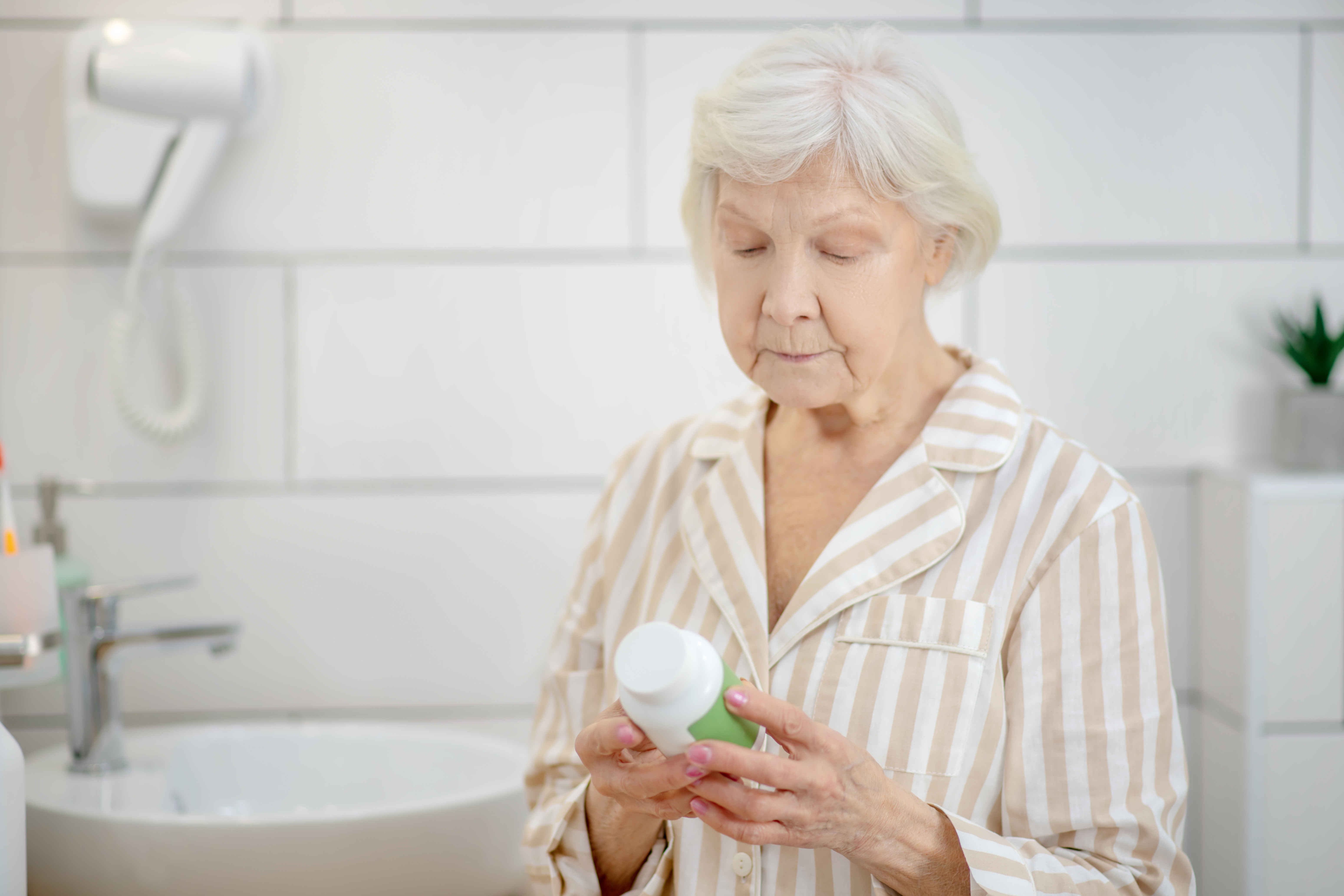 Short-haired old lady holding a bottle with vitamins in her hands